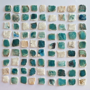 May include: A collection of small, square ceramic tiles in shades of teal, white, and beige. The tiles have a textured, uneven surface and are arranged in a grid. Some tiles have a speckled or mottled appearance, creating a varied aesthetic.
