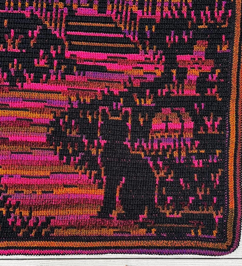 Op de afbeelding: Een gehaakte deken met een zwart katten silhouet tegen een levendige achtergrond. Het ontwerp bevat tinten roze, oranje en paars, waardoor een gepixeleerd effect ontstaat. De deken heeft een donkere rand.