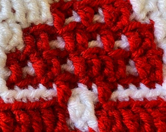 May include: Close-up of a red and white crocheted square with a textured pattern.