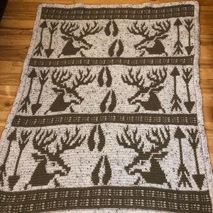 May include: A crocheted throw blanket with a white background and brown deer, arrow, and footprint designs.