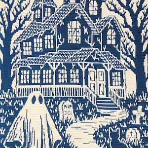 Op de afbeelding: Een blauw-witte gehaakte Halloween-sc&egrave;ne met een spookhuis, een geest, een zwarte kat en een begraafplaats. Het huis heeft meerdere ramen en een veranda. Bomen omlijsten het huis. De geest staat op de voorgrond en de kat staat bij de begraafplaats.