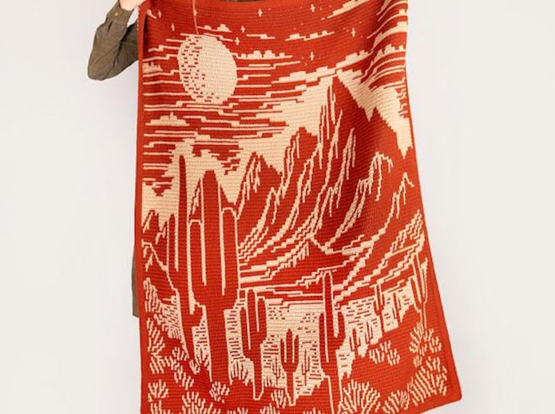 Peut inclure: Une couverture en crochet avec un motif de paysage d&eacute;sertique. La couverture pr&eacute;sente une grande pleine lune, des montagnes et des cactus dans des tons d'orange et de cr&egrave;me.