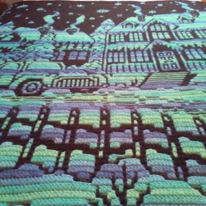 May include: A crocheted blanket with a winter scene featuring a house, a car, and a fence. The blanket is made with blue, green, and purple yarn.