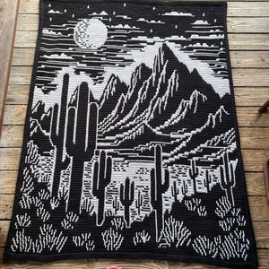 Peut inclure: Couverture en crochet noir et blanc avec un motif de paysage d&eacute;sertique. La couverture repr&eacute;sente une cha&icirc;ne de montagnes, une pleine lune et des cactus.