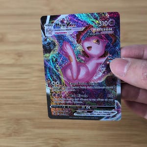 May include: A holographic Mew VMAX Fusion Strike trading card. The card features a pink Mew character with the text "Mew VMAX" and "Fusion Strike". The card has a 310 HP rating and the attack "Cross Fusion Strike".
