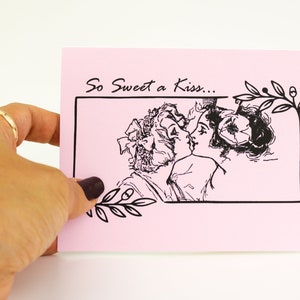 May include: A pink greeting card with the text "So Sweet a Kiss..." above a black and white illustration of two people kissing. The card has a black border and decorative floral elements.