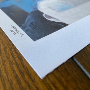 May include: A white paper print with a blue and gray abstract painting. The print is signed "Sarah's Art" and dated "03/22".