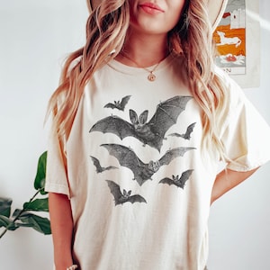 May include: A white oversized t-shirt with a graphic print of bats in flight. The shirt is made of a soft, comfortable material and has a relaxed fit.