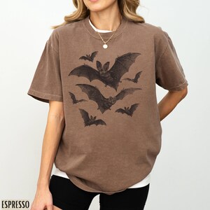 May include: A brown t-shirt with a graphic print of bats flying in a group. The bats are black and white and have a vintage look.