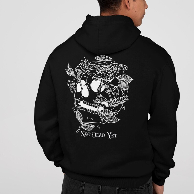May include: Black hooded sweatshirt with a white graphic of a skull, mushrooms, and leaves. The text "NOT DEAD YET" is below the skull design. The sweatshirt is made of a soft material.