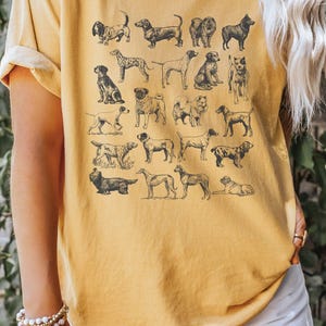 May include: A yellow t-shirt with a vintage illustration of various dog breeds printed on the front. The shirt has a relaxed fit and short sleeves.