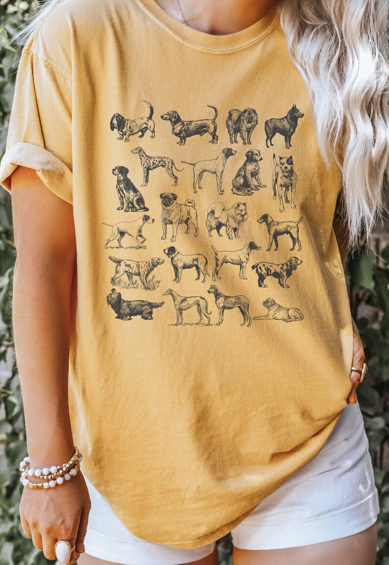 May include: A yellow t-shirt with a vintage illustration of various dog breeds printed on the front. The shirt has a relaxed fit and short sleeves.