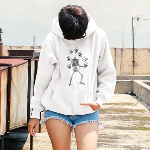 May include: White hooded sweatshirt featuring a graphic of a skeleton juggling skulls.