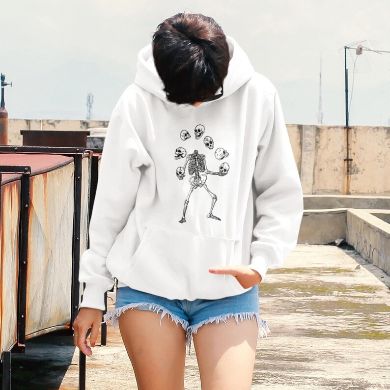 May include: White hooded sweatshirt featuring a graphic of a skeleton juggling skulls.