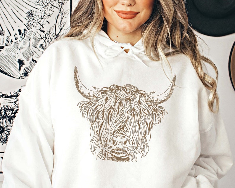 May include: A white hoodie with a brown line drawing of a Highland cow with long, shaggy hair and horns.