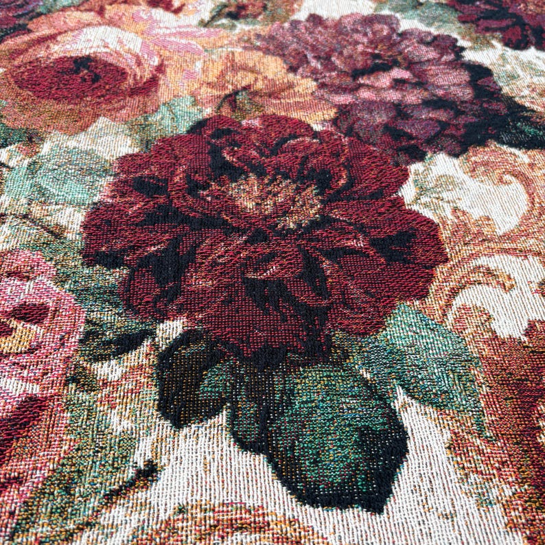 May include: Close-up of a floral tapestry featuring large, detailed roses in shades of burgundy, pink, and peach. The leaves are a mix of green and black. The background has a cream-colored, ornate pattern.