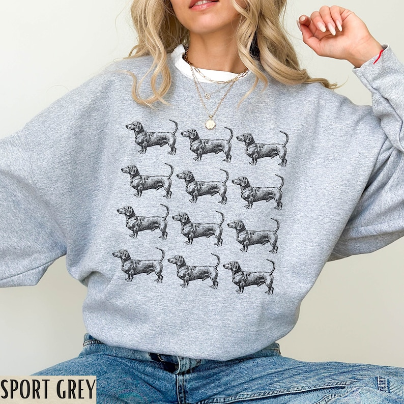 Peut inclure: Un sweat-shirt gris avec un motif r&eacute;p&eacute;t&eacute; de chiens teckels noirs. Le sweat-shirt a un col rond et des manches longues.