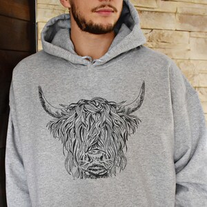 May include: A gray hooded sweatshirt with a black and white illustration of a Highland cow on the front.