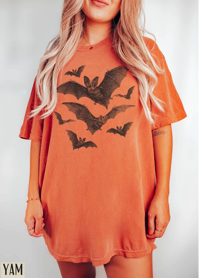 May include: A burnt orange oversized t-shirt with a graphic print of bats in flight. The bats are black and white and have a vintage illustration style.