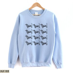 Peut inclure: Sweat-shirt bleu clair avec un motif de chiens teckels noirs.