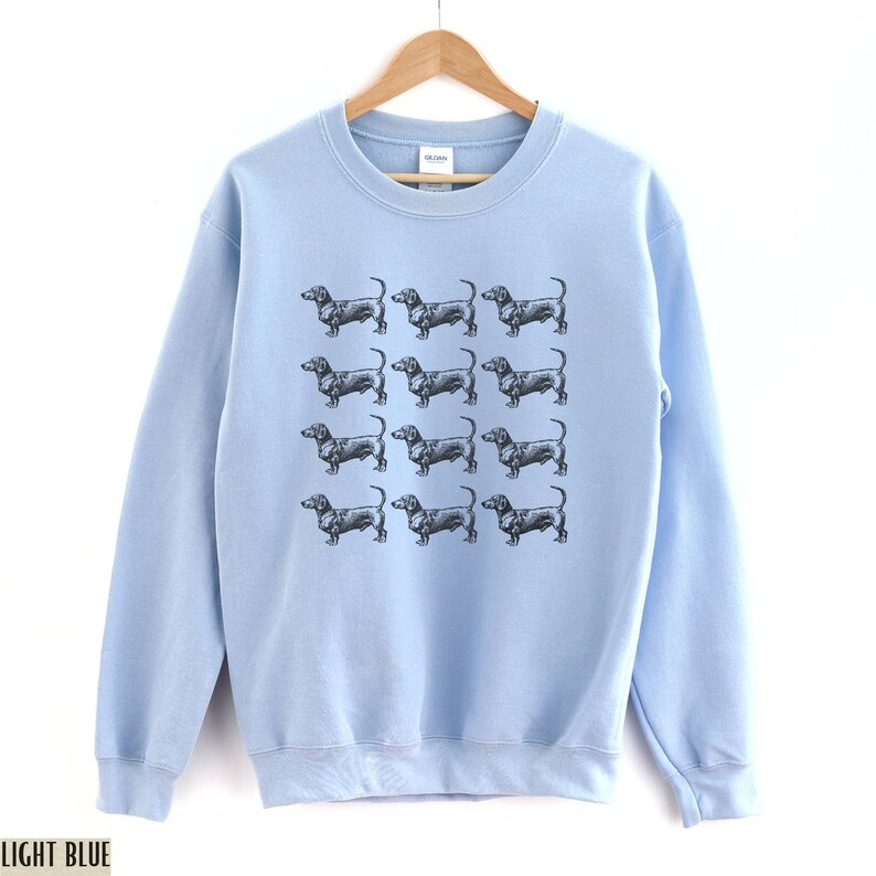 Peut inclure: Sweat-shirt bleu clair avec un motif de chiens teckels noirs.