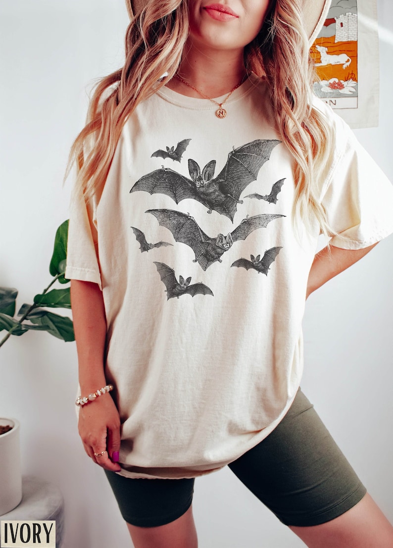 May include: A white oversized t-shirt with a graphic print of bats in flight. The shirt is made of a soft, comfortable material and has a relaxed fit.