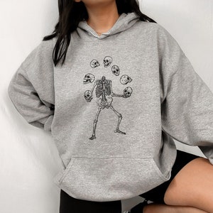 May include: Grey hooded sweatshirt with a black graphic of a skeleton juggling skulls.