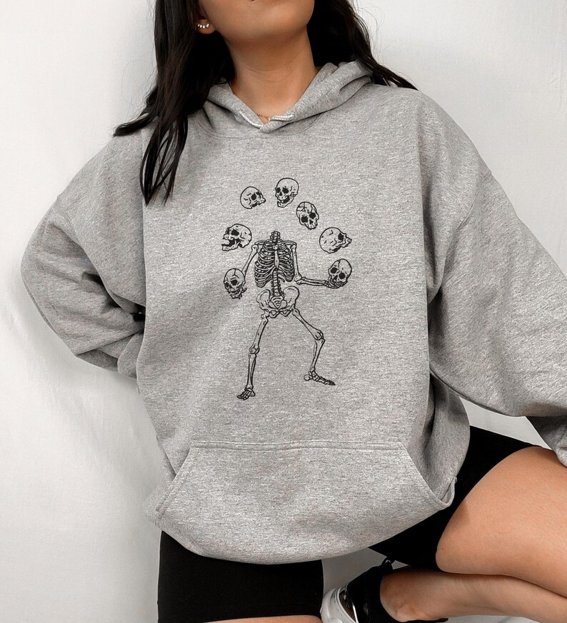 May include: Grey hooded sweatshirt with a black graphic of a skeleton juggling skulls.