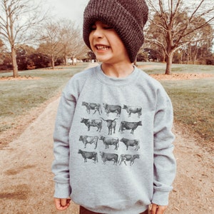 May include: A gray sweatshirt with a vintage-style print of cows. The sweatshirt has a crew neck and long sleeves.