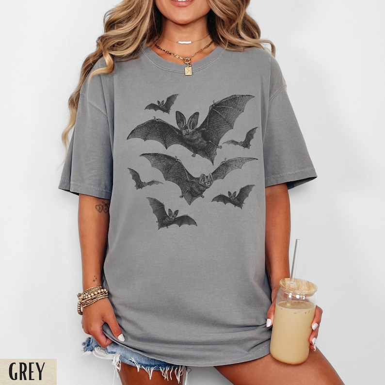 May include: A grey t-shirt with a graphic print of bats in a vintage style. The shirt has a relaxed fit and a crew neck.