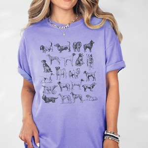 May include: A purple t-shirt with a graphic print of various dog breeds in black and white. The shirt has a crew neck and short sleeves.