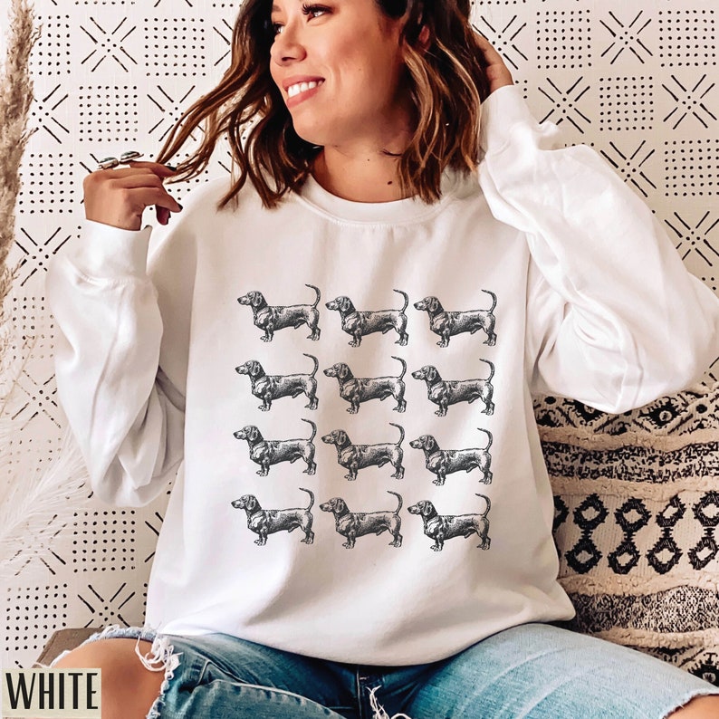 Peut inclure: Sweat-shirt blanc avec un motif r&eacute;p&eacute;t&eacute; d'illustrations de teckels noirs et blancs.