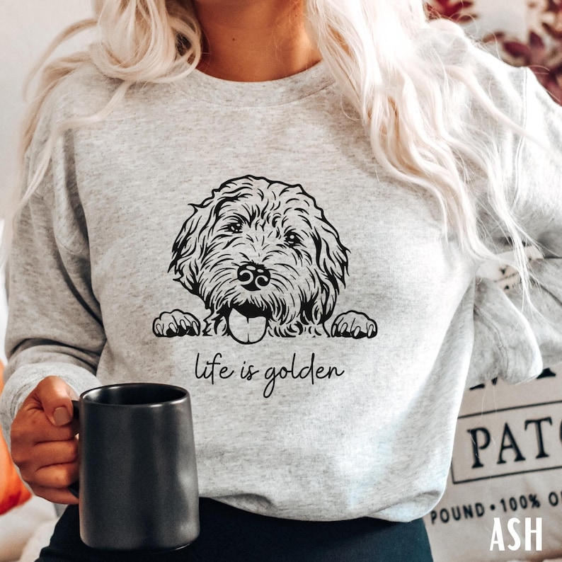 以下が含まれることがあります： グレーのトレーナーに、犬が上の方から顔を出している白黒のイラストが描かれています。犬の下には「life is golden」という文字が印刷されています。