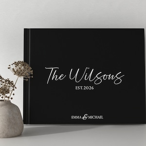 May include: Black photo album with white text that reads "The Wilsons Est. 2026 Emma & Michael"