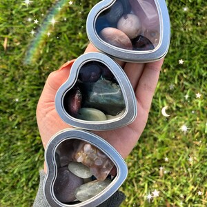May include: Three heart-shaped metal tins with clear lids, each filled with a variety of colorful stones and crystals.