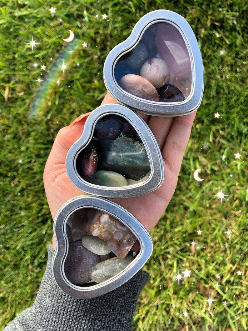 May include: Three heart-shaped metal tins with clear lids, each filled with a variety of colorful stones and crystals.