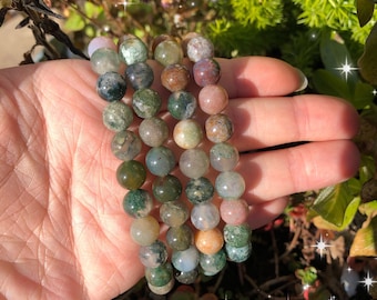 May include: Three stacked bracelets made of moss agate beads. The beads are a mix of green, brown, and pink.