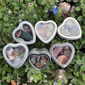 May include: Six heart-shaped metal tins with clear lids, each filled with a variety of colorful crystals and gemstones.