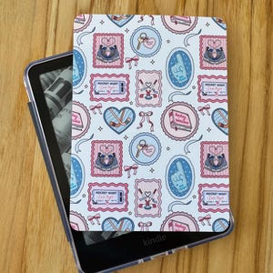 May include: A Kindle e-reader with a patterned cover featuring pink, blue, and white designs. The cover includes illustrations of hockey-themed elements such as skates, tickets, and hearts. The text "HOCKEY NIGHT" is visible on the cover.