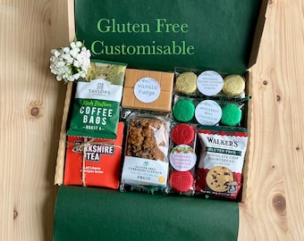 Può includere: Una scatola regalo verde piena di prelibatezze senza glutine, tra cui bustine di caffè, tè, fudge, biscotti e creme al cioccolato. La scatola è etichettata "Gluten Free Customisable".