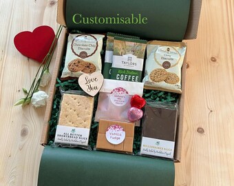 May include: A gift box filled with various treats, including biscuits, coffee, fudge, and chocolate hearts. The box is green and has the word "Customisable" printed on it. A red heart and white flowers are placed next to the box.