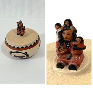 May include: A small, round, beige ceramic jar with a lid, featuring a Native American design. The jar has a black and red geometric pattern around the middle and a small figurine on top. The figurine depicts a woman with children.