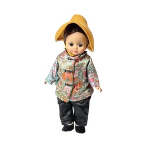 May include: A vintage doll wearing a straw hat and traditional Asian-inspired clothing. The doll's outfit includes a patterned jacket with black pants and shoes. The doll has dark hair and is set against a white background.