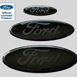 Puede incluir: Tres emblemas Ford ovalados negros con un acabado metálico plateado. Los emblemas son de diferentes tamaños. El emblema más grande está en la parte inferior, el emblema de tamaño mediano está en el medio y el emblema más pequeño está en la parte superior.