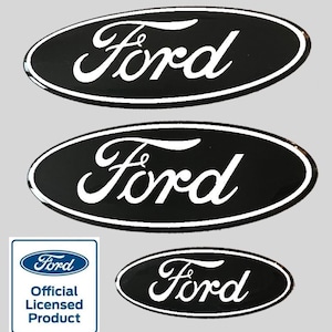 Op de afbeelding: Drie zwarte ovale Ford-emblemen met witte letters. Het grootste embleem bevindt zich bovenaan, gevolgd door een kleiner embleem, en het kleinste embleem bevindt zich onderaan. Het kleinste embleem bevindt zich naast een blauw vierkant met het Ford-logo en de tekst "Officieel gelicentieerd product".