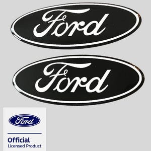 Puede incluir: Dos emblemas ovalados de color negro con el logotipo de Ford en blanco y un borde blanco. Debajo de los emblemas hay una etiqueta cuadrada blanca con el logotipo azul de Ford y el texto Official Licensed Product en letras azules y negras.