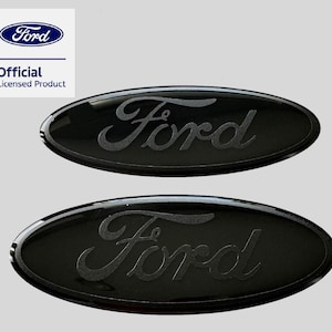 May include: Two oval-shaped black Ford emblems with a glossy finish and matte black script lettering. The Ford logo is centred on each piece. A white square in the top left corner displays the blue Ford logo and the text Official Licensed Product.
