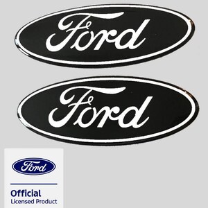 May include: Two oval-shaped black emblems featuring the white Ford script logo with a white border. Below the emblems is a square white label with the blue Ford logo and the text Official Licensed Product in blue and black lettering.