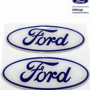 Peut inclure: Deux autocollants ovales avec le logo Ford, présentant l'écriture bleue classique sur fond blanc avec une bordure bleue. Le coin supérieur droit contient un petit rectangle avec le logo Ford et le texte Official Licensed Product.