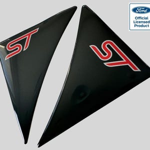 Pode incluir: Dois adesivos triangulares pretos para janelas de carro com um logotipo "ST" vermelho. Os adesivos são produtos oficiais licenciados pela Ford.